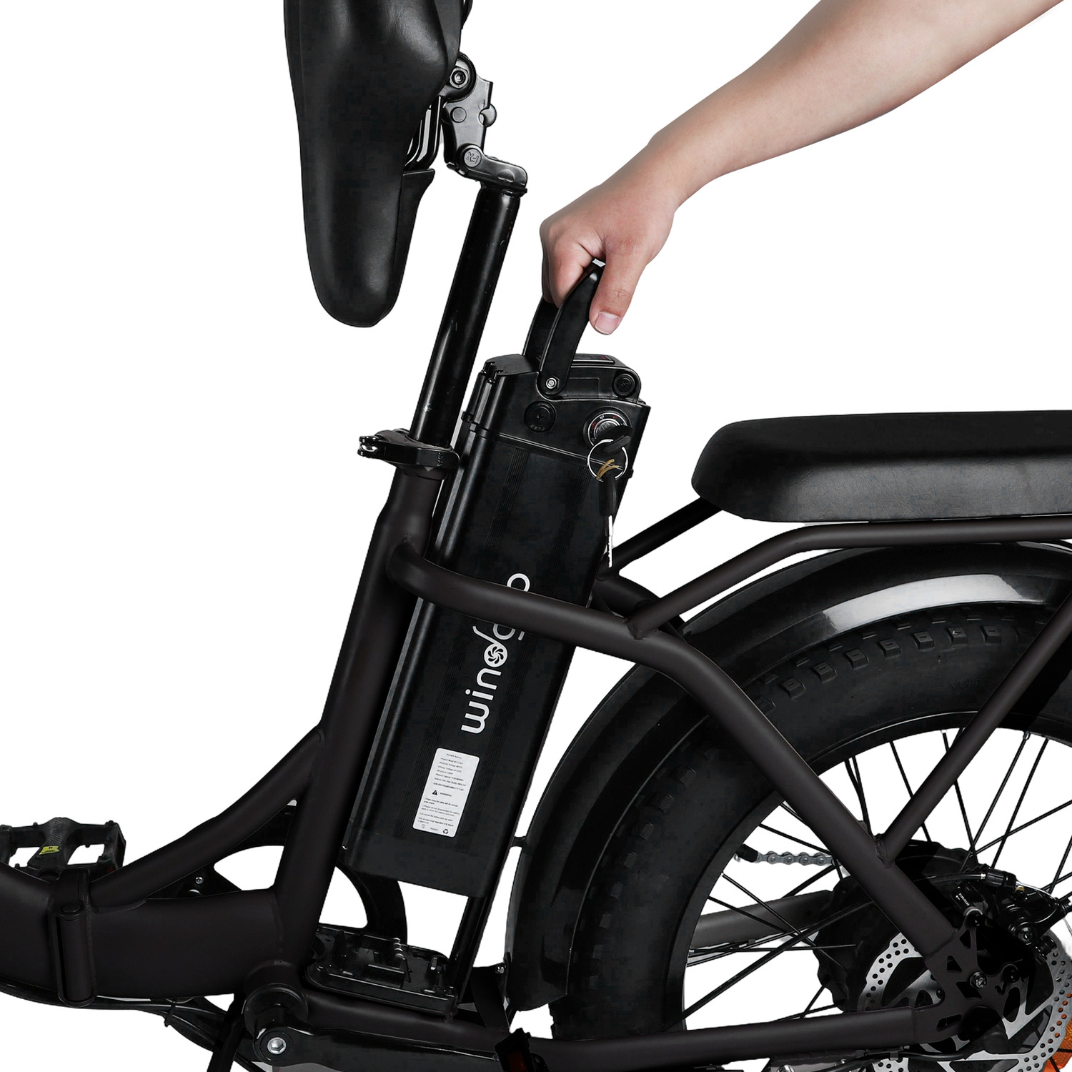 Een hand houdt de handgreep van de accu van een zwarte elektrische fiets vast. De zitting en het frame zijn ook zwart.