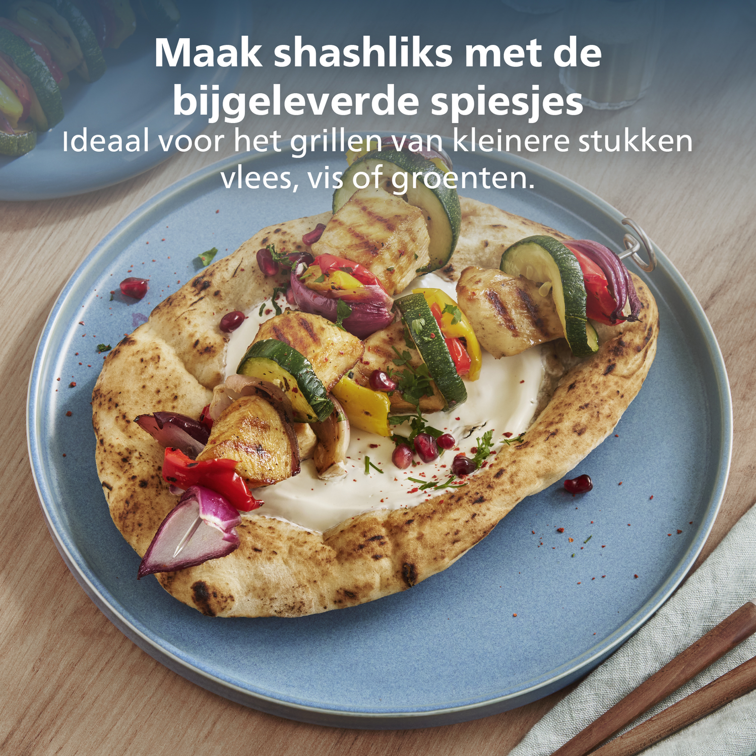 Brochettes grillées avec légumes et poulet sur pain pita, servies sur une assiette bleue. Table en bois et serviette en arrière-plan.