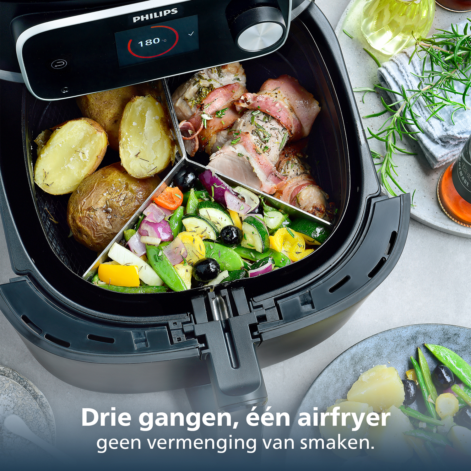 An air fryer with potatoes, meat wrapped in bacon, and vegetables. The fryer has a digital display showing 180 degrees.