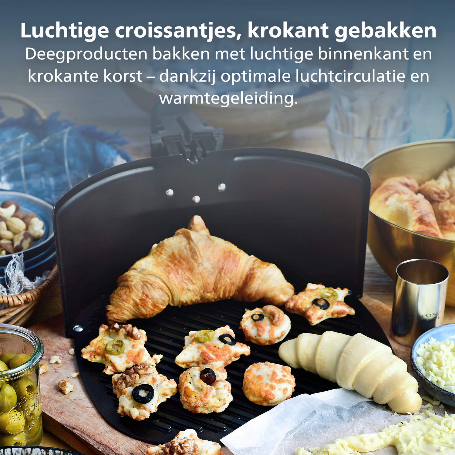 Gros plan sur des produits de boulangerie, dont des croissants et des pâtisseries garnies, sur un grill noir. Divers ingrédients les entourent.