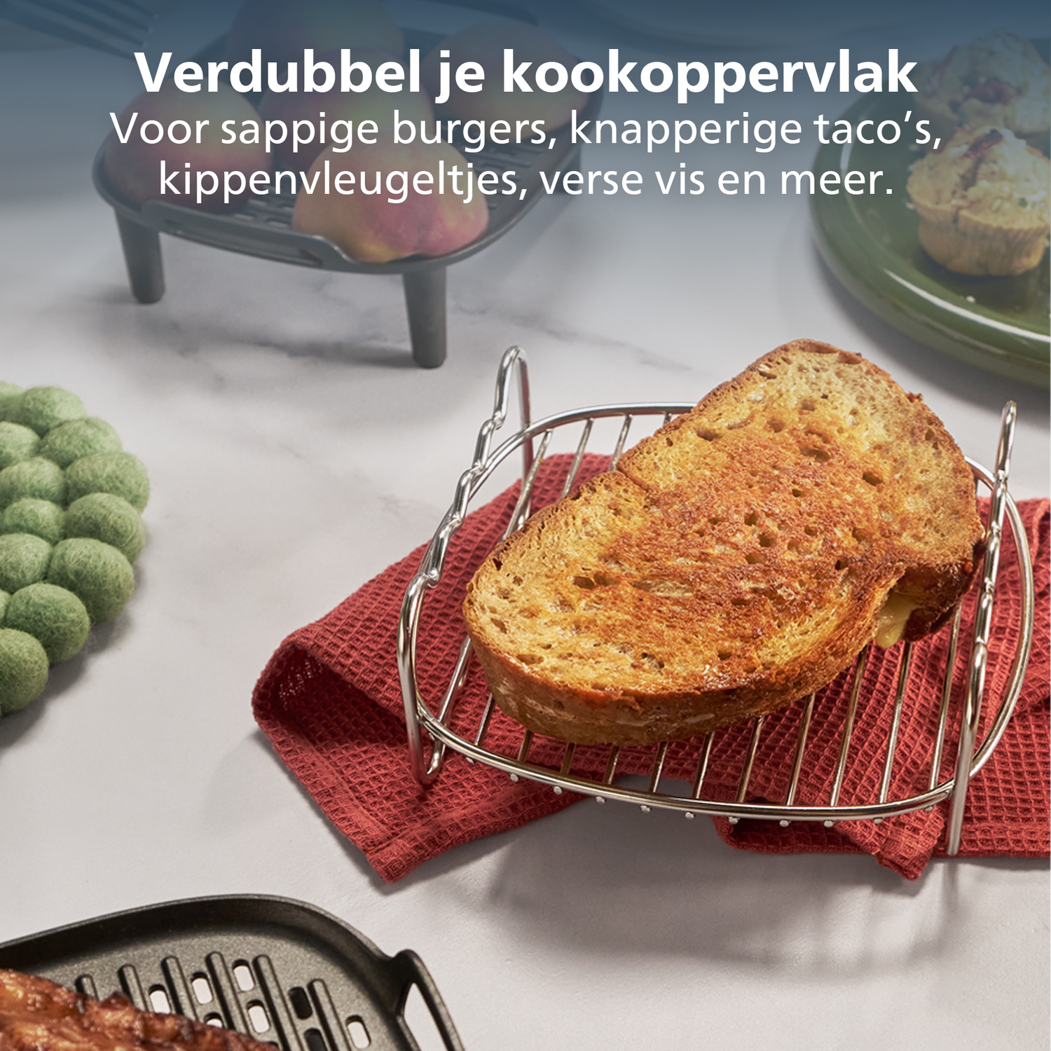 Een sneetje geroosterd brood op een zilveren rekje boven een rode doek. Op de achtergrond een zwarte grill en een groen bord met eten.