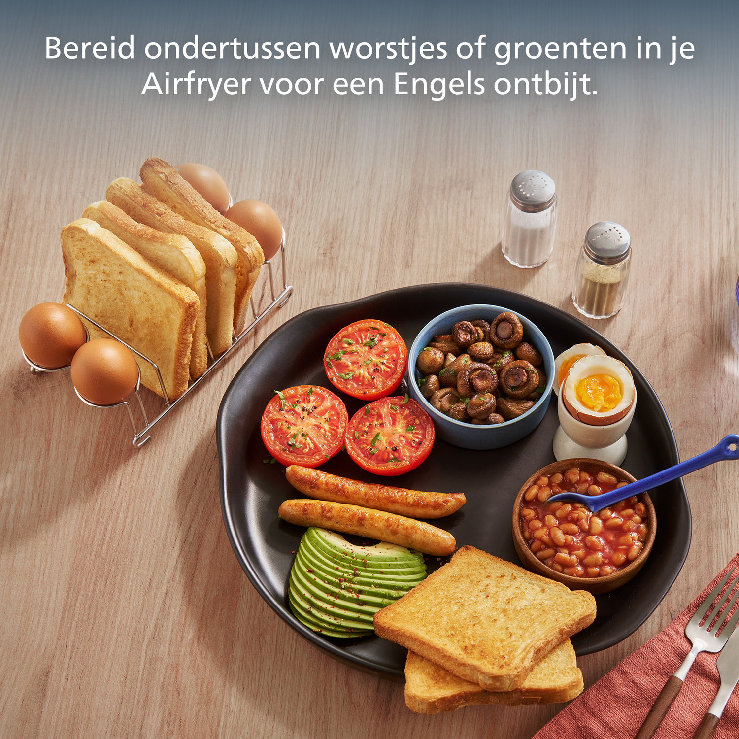 Engels ontbijt met toast, eieren, tomaten, champignons, bonen, avocado en worstjes op een zwart bord. Zout- en peperstrooiers.
