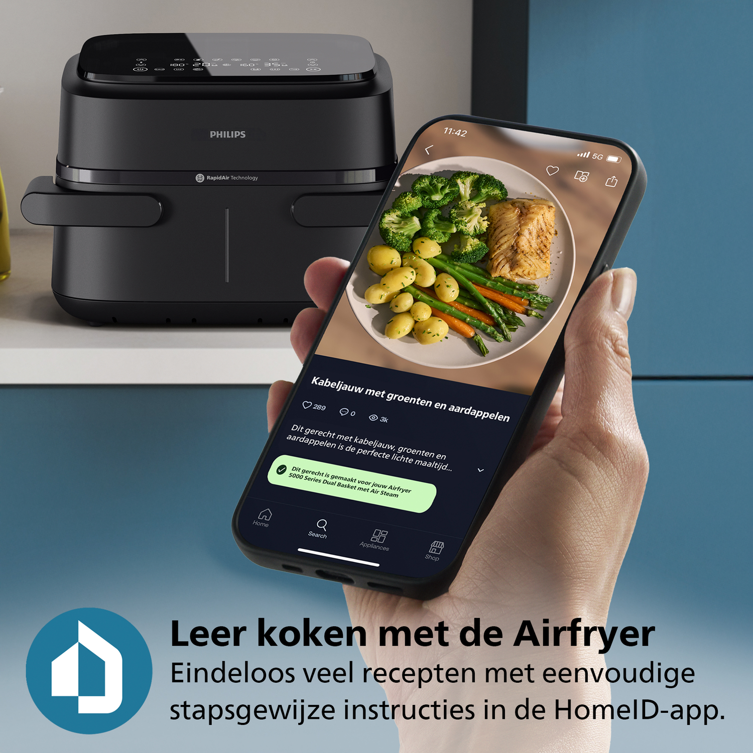 Een zwarte Philips airfryer naast een telefoon met een maaltijd van vis, groenten en aardappelen. Op de telefoon staat 'Kabeljauw'.