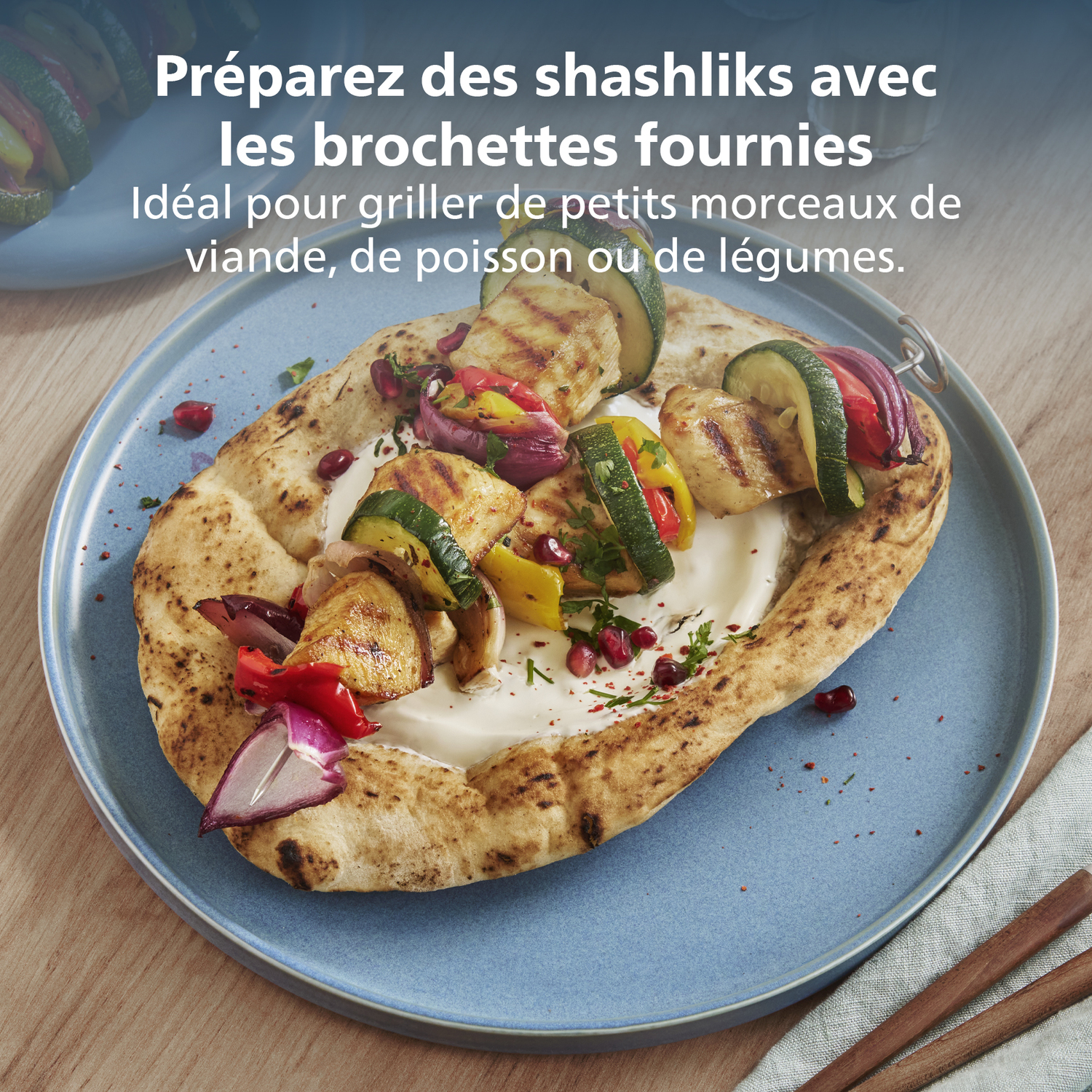 Chachlik grillé sur pain pita, avec légumes et sauce sur une assiette bleue. Table en bois avec texte en français.