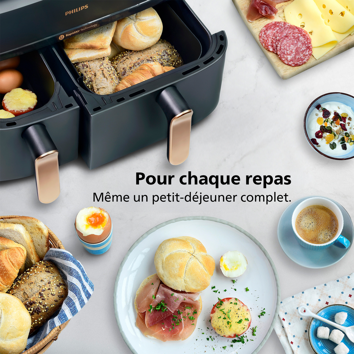 Un airfryer avec divers aliments pour le petit-déjeuner : pain, œufs, yaourt, café, fromage, salami et petits pains. Une scène complète.