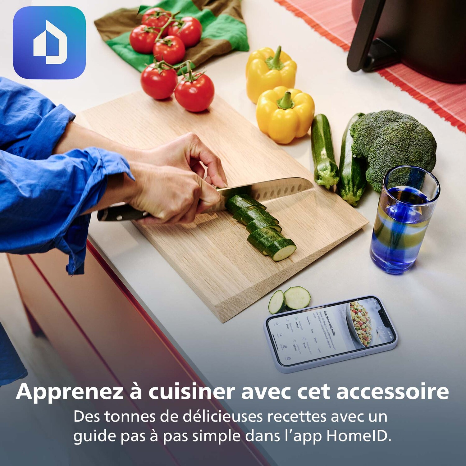 Een persoon snijdt courgette op een houten plank. Tomaten, paprika's en broccoli zijn in de buurt. Een telefoon toont een recept.
