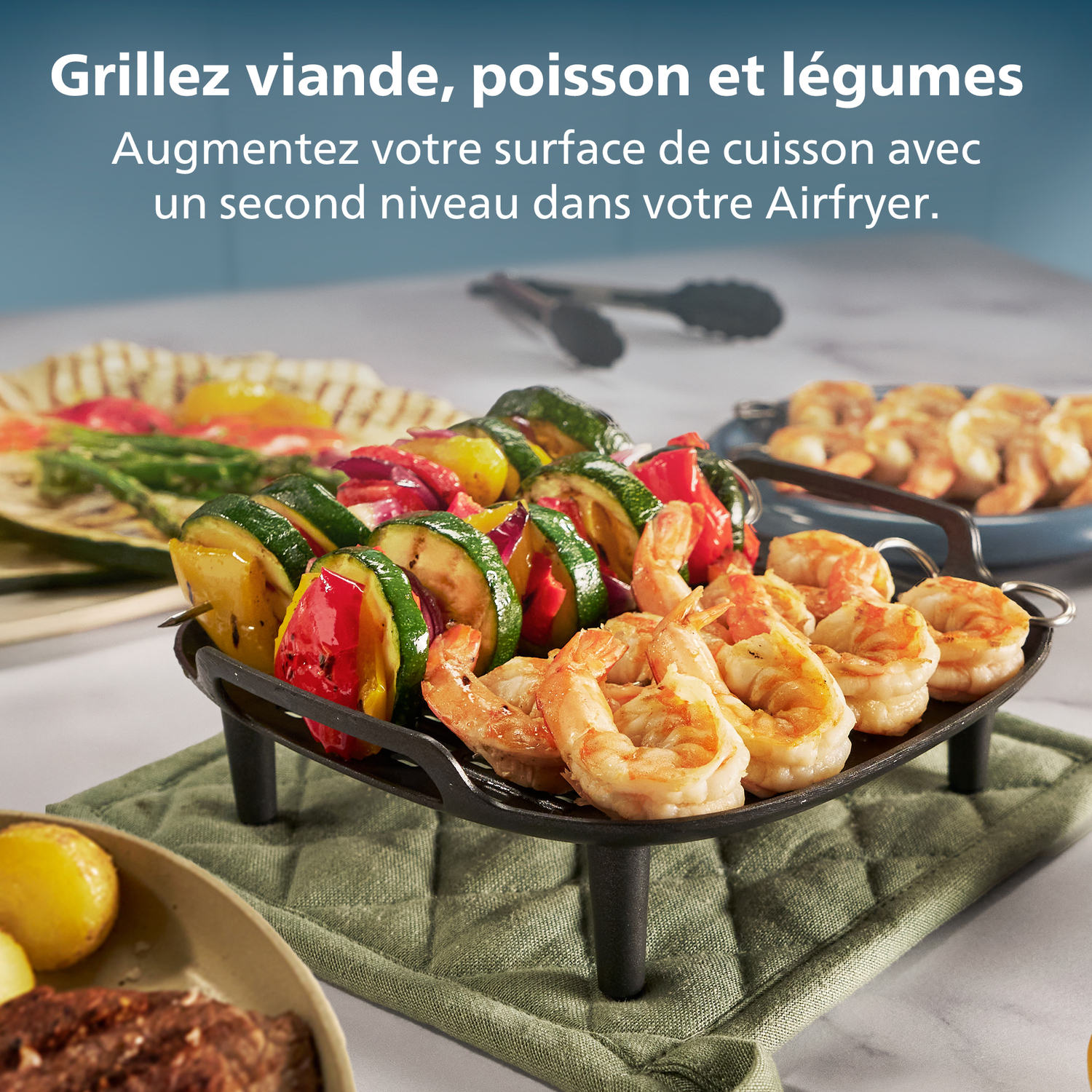 Gegrilde groenten en garnalen op een zwarte grill. Andere gerechten met eten staan op de achtergrond. Groene pannenlappen zijn zichtbaar.