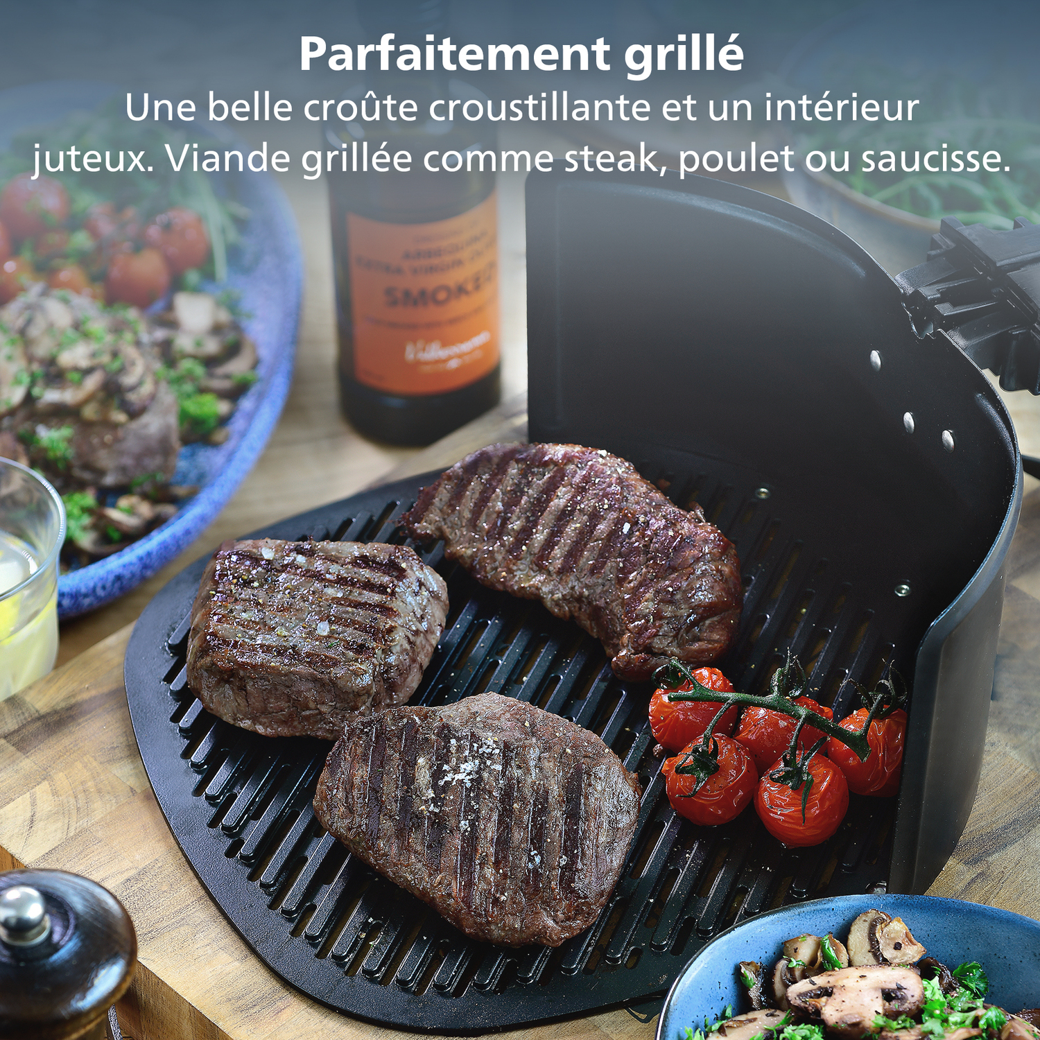 Steaks grillés et tomates sur un grill. D'autres plats sont dans des bols bleus. Une bouteille d'huile fumée est en arrière-plan.