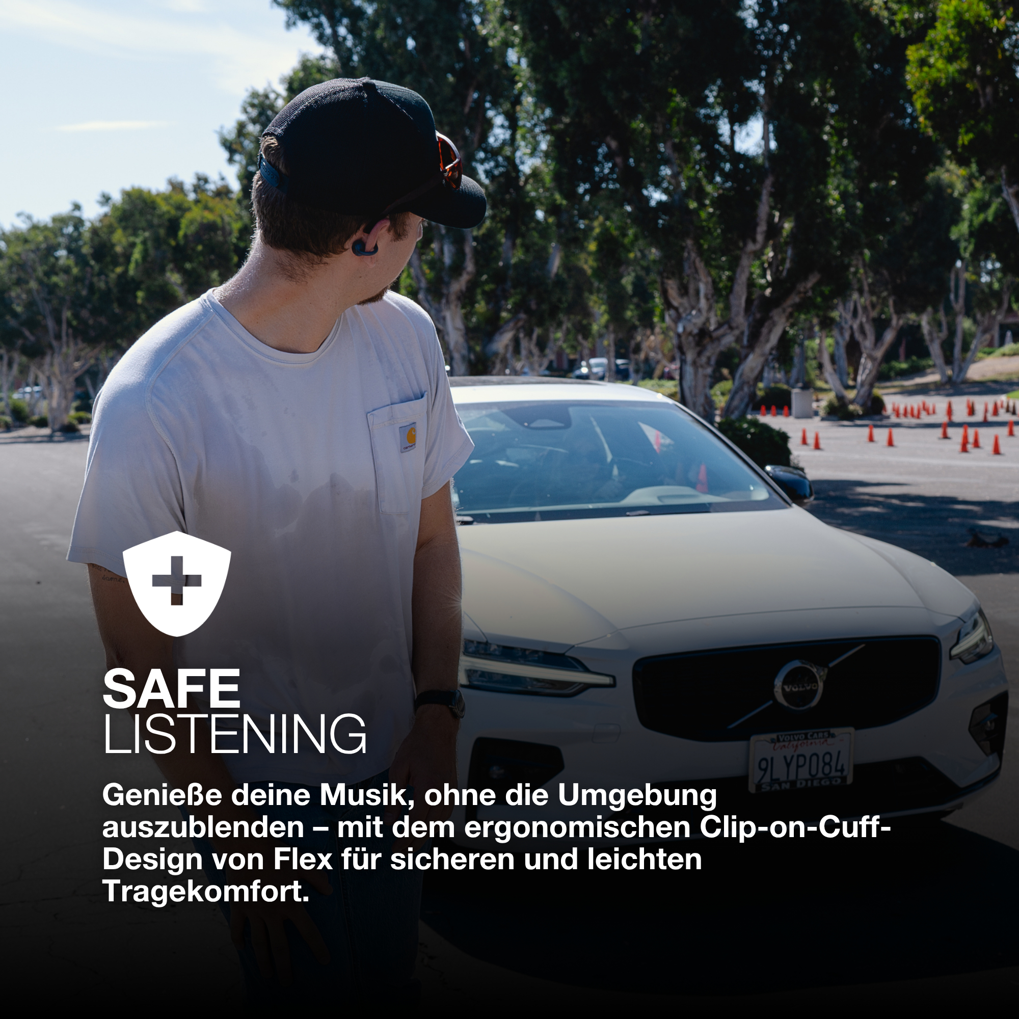 Mann mit Kappe und weißem Hemd blickt auf ein weißes Auto. Bäume im Hintergrund. Text: Sicheres Hören, Musik ohne Ablenkung genießen.