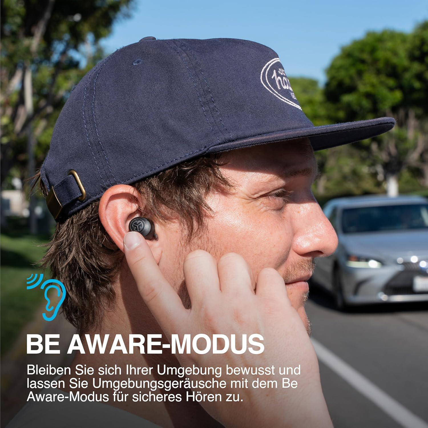 Ein Mann mit marineblauer Kappe und Ohrhörern im Ohr. Im Hintergrund ein Auto. Text: BE AWARE-MODUS.