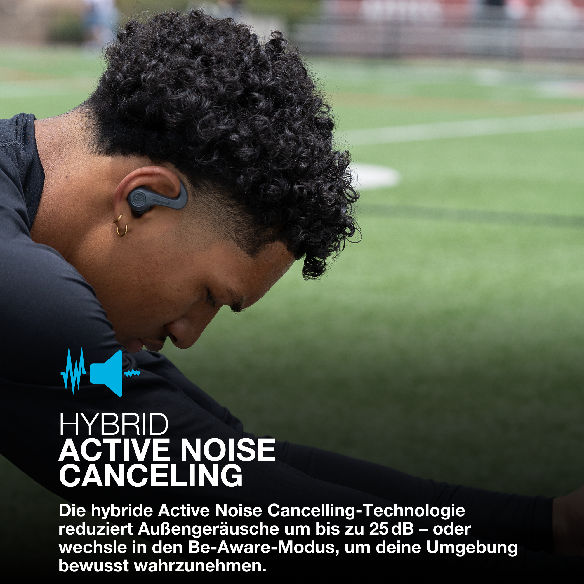 Ein Mann mit Kopfhörern dehnt sich auf einem grünen Feld. Das Bild wirbt für hybride Active Noise Cancelling-Technologie.