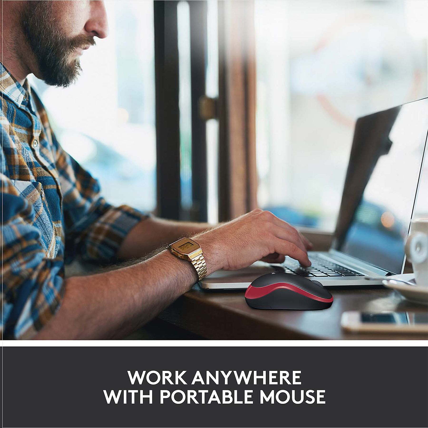 Un uomo con la barba lavora su un laptop, usando un mouse nero e rosso. Lo sfondo presenta una finestra e una tazza di caffè.