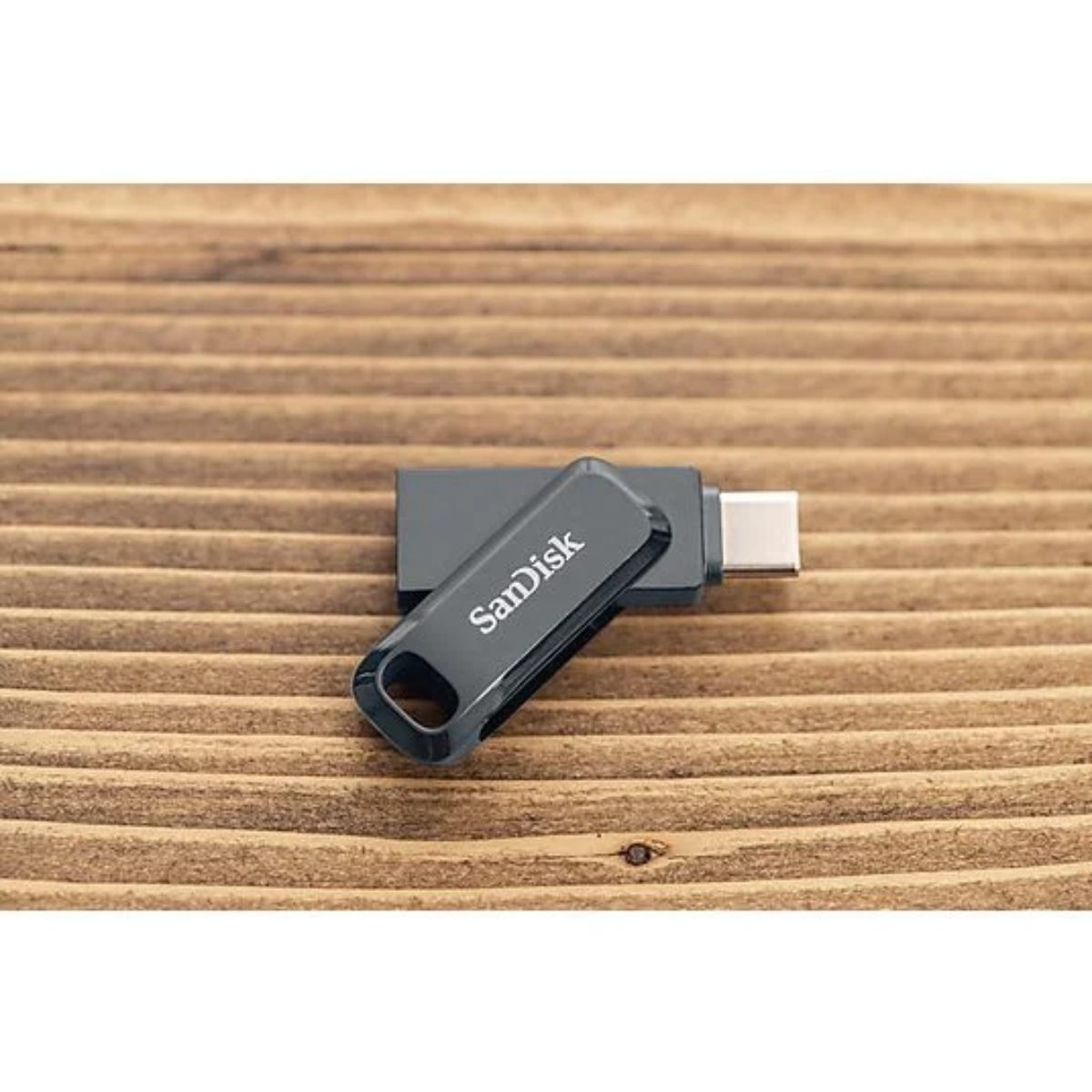 Una memoria USB SanDisk negra está sobre una superficie de madera. La unidad está abierta, revelando el puerto USB-C.