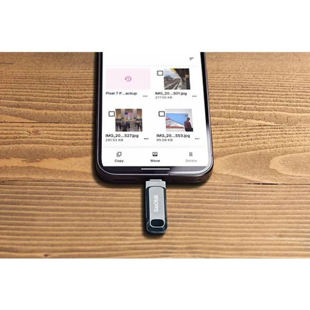 Un teléfono inteligente muestra una interfaz de gestión de archivos, conectado a una unidad USB SanDisk. Descansa sobre una superficie de madera.