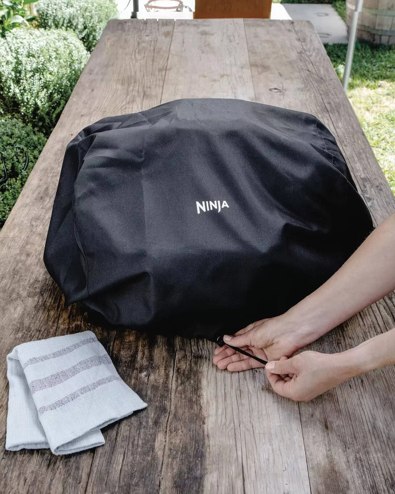 Una cubierta negra de Ninja sobre una mesa de madera. Manos tirando del cordón. Una toalla doblada está sobre la mesa.