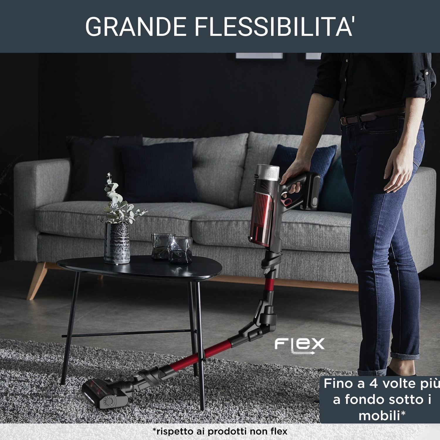 Una persona tiene in mano un aspirapolvere flessibile. Sullo sfondo un divano, un tavolo e un tappeto. Il testo dice "Grande Flessibilita'".
