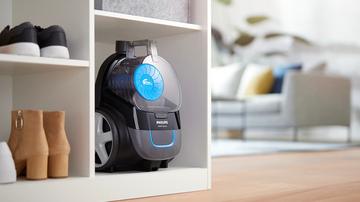 Czarny i szary odkurzacz Philips stoi w białej szafce. Buty na półkach powyżej i buty poniżej.