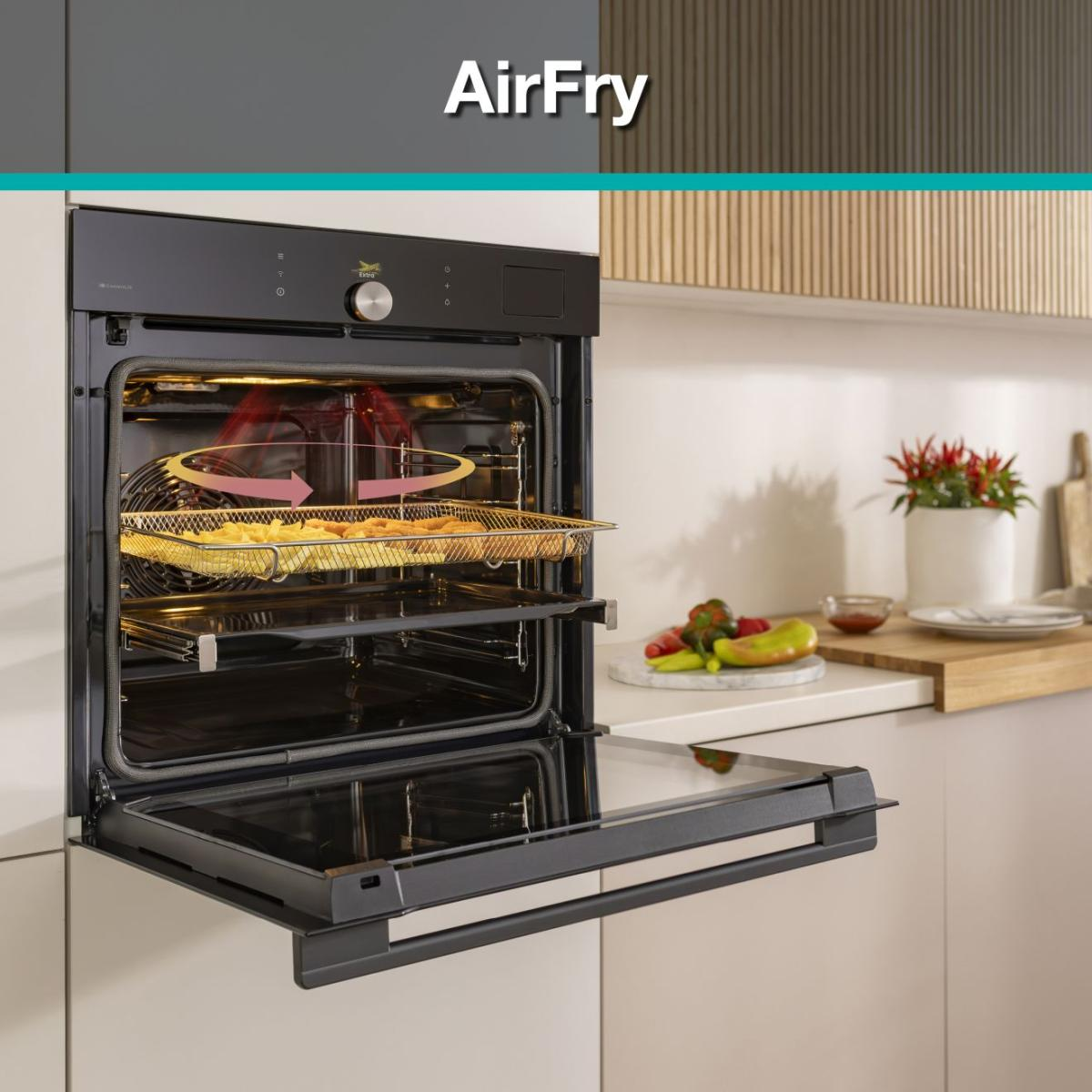 Czarny piekarnik z frytkownicą powietrzną z otwartymi drzwiami. Jedzenie na drucianym ruszcie w środku. Blat kuchenny z warzywami i rośliną w tle.