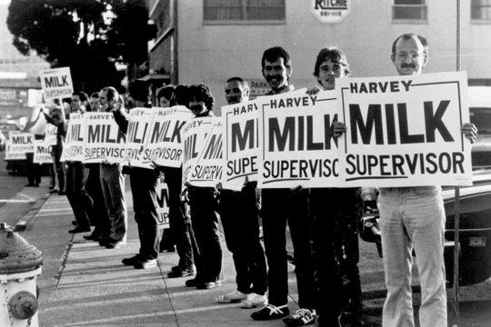 Ein Schwarz-Weiß-Foto zeigt eine Gruppe von Menschen, die Schilder mit der Aufschrift 'Harvey Milk Supervisor' halten.