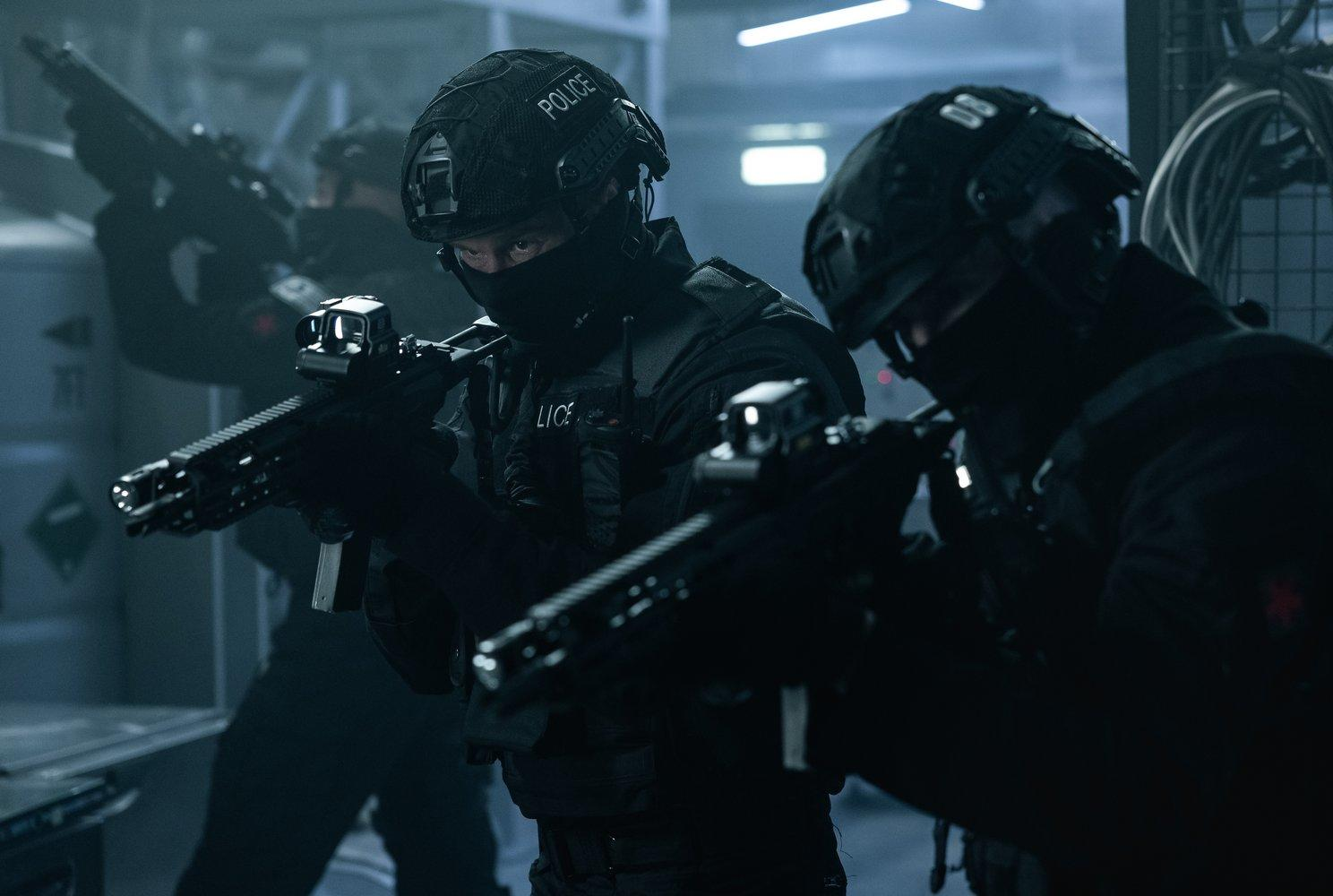 SWAT-Teammitglieder in schwarzer taktischer Ausrüstung zielen mit Gewehren. Auf einem Helm steht 'POLIZEI'. Dunkle, industrielle Umgebung.