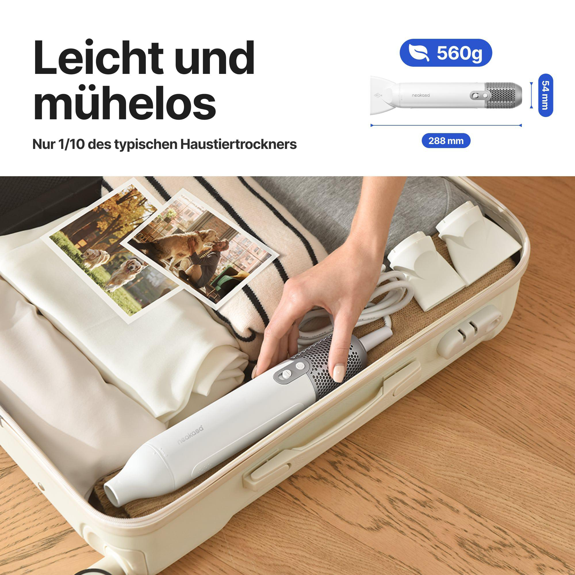 Ein weißer Haustiertrockner liegt in einem offenen Koffer mit Kleidung und Fotos. Eine Hand greift danach.