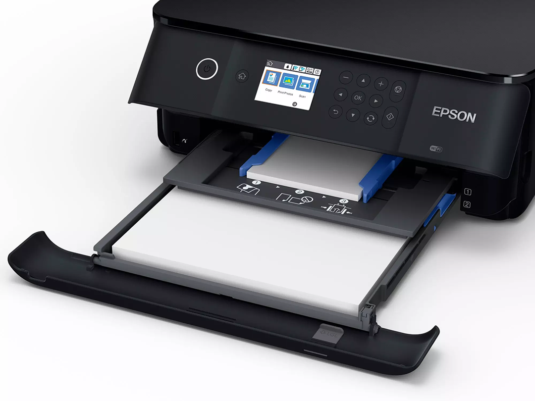 Egy fekete Epson nyomtató nyitott papírtálcával. A tálca fehér papírt tartalmaz. A nyomtatón van egy vezérlőpanel és egy WiFi logó.
