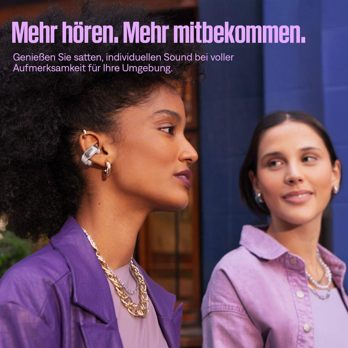 Zwei Frauen mit Schmuck, eine in lila Jacke, die andere in rosa Hemd, vor blauem Hintergrund. Text: Mehr hören. Mehr mitbekommen.