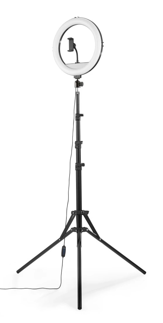 Lampa pierścieniowa na statywie jest wyświetlana na białym tle. Lampa pierścieniowa jest włączona, a pośrodku znajduje się uchwyt na telefon.