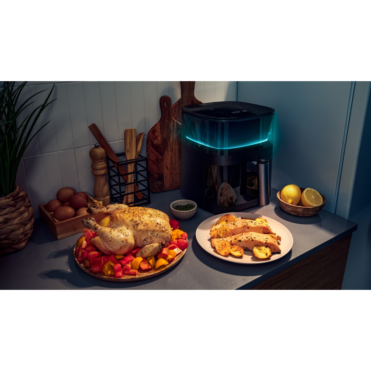 Una scena di cucina mostra un pollo arrosto, salmone e una friggitrice ad aria. Sono presenti anche verdure e limoni. La scena è ben illuminata.