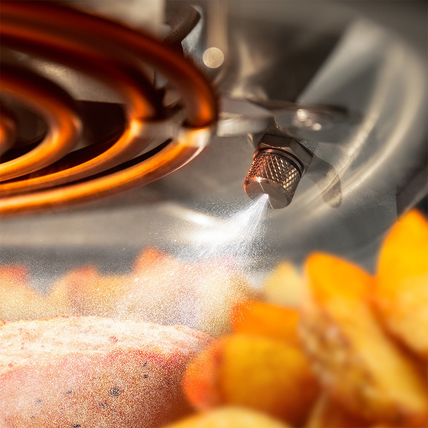 Un ugello spruzza nebbia. Bobine di rame sullo sfondo. Pesche in primo piano, creando un colore arancione e giallo sfocato.