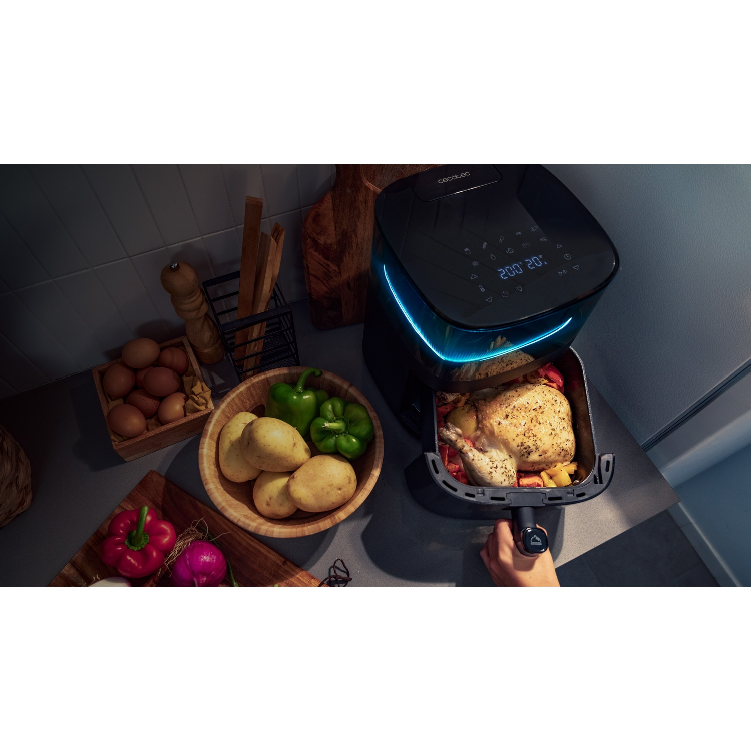Una friggitrice ad aria con un pollo cotto all'interno. Verdure e uova sono accanto. La friggitrice è nera e il pollo è dorato.