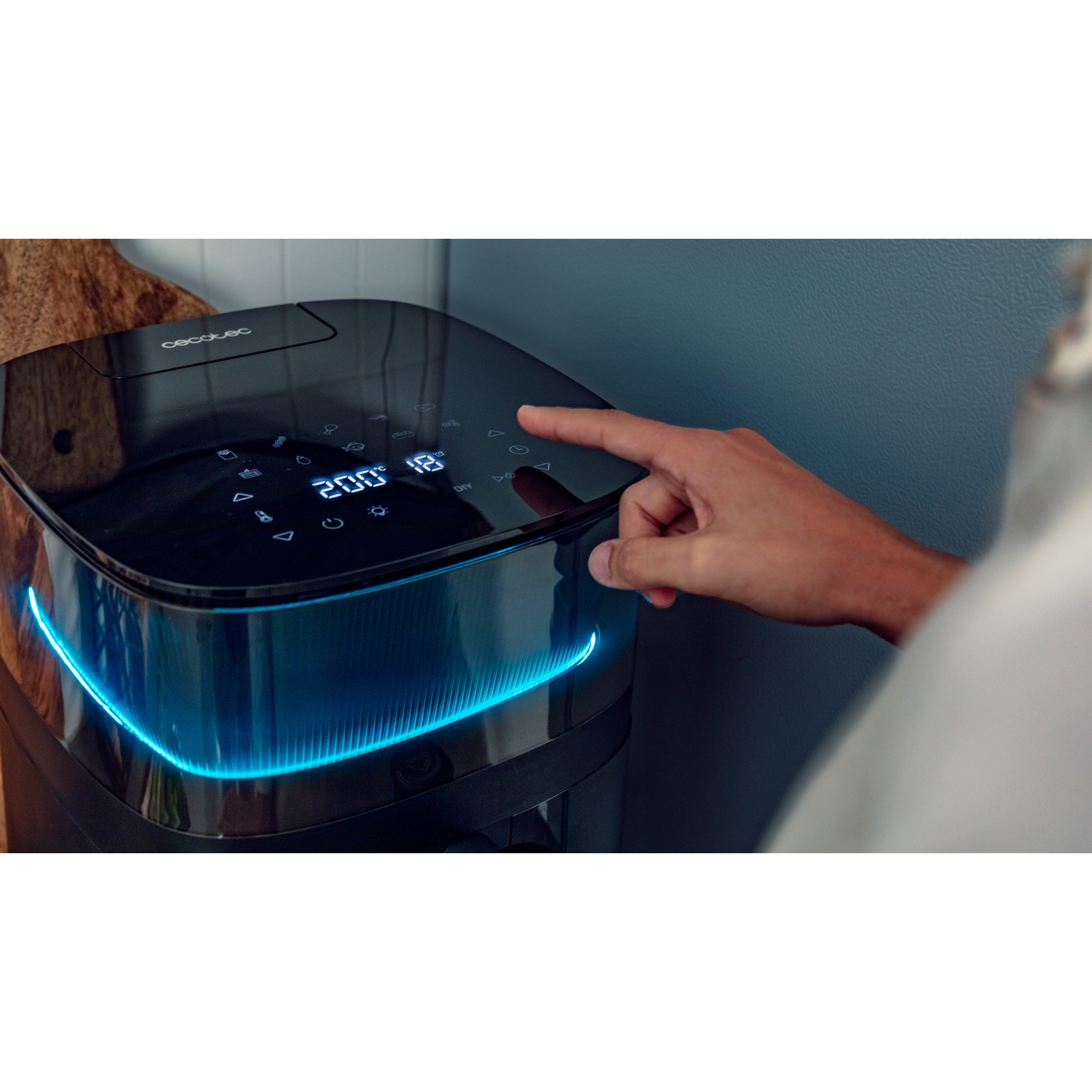 Una friggitrice ad aria nera con luce blu. Una mano tocca lo schermo. Il display mostra 200° e 18.