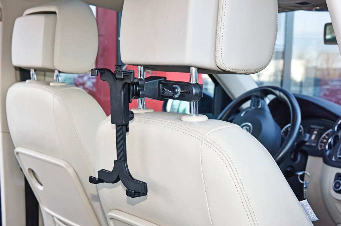 Widok wnętrza samochodu. Czarny uchwyt na tablet jest zamontowany na kremowym fotelu samochodowym. Kierownica widoczna w tle.