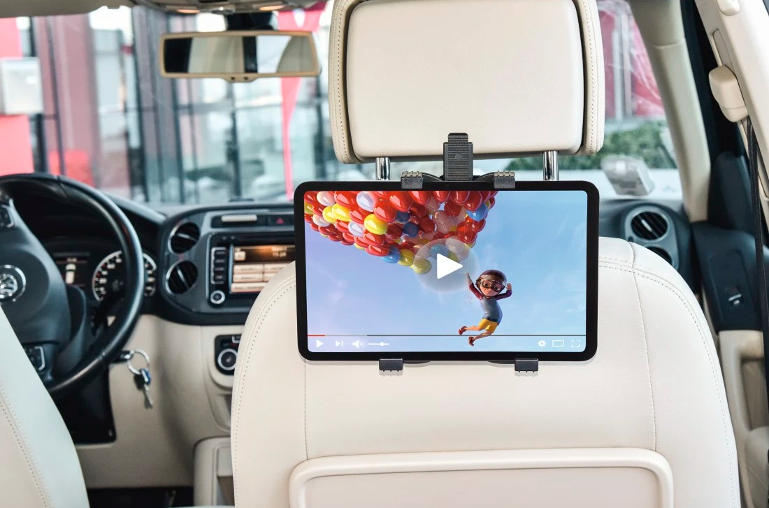 Tablet z kreskówką dziecka z balonami, zamontowany na siedzeniu samochodowym. Widoczne wnętrze samochodu.