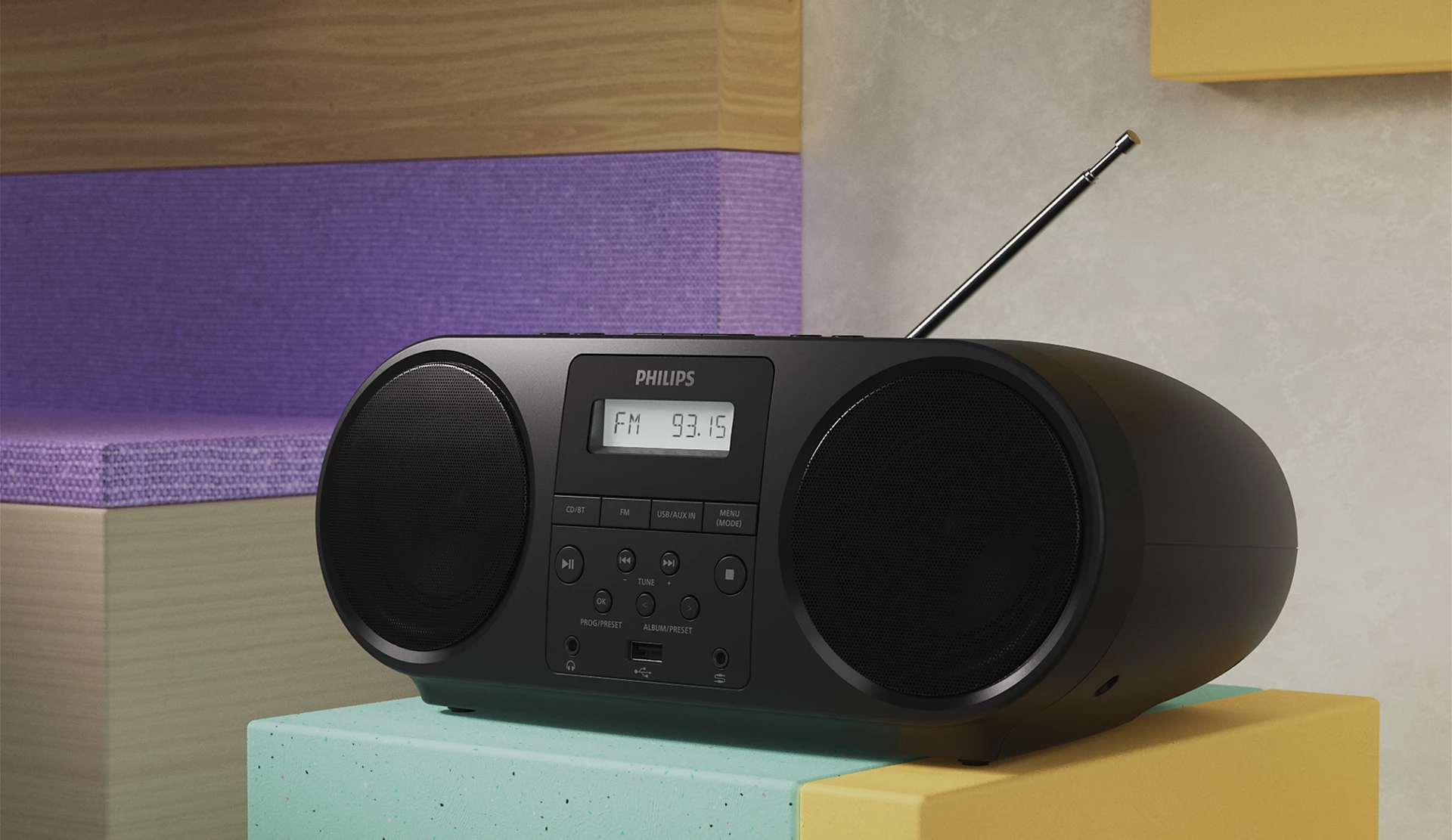 Fekete Philips rádió boombox hangszórókkal. FM 93.15-öt jelenít meg. Világoszöld és kék tömbön van. A háttér lila és sárga tömbökből áll.