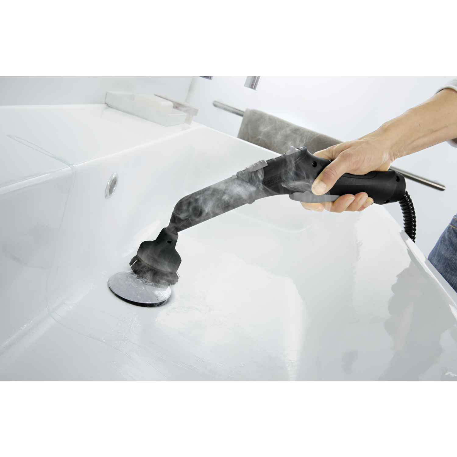 A person is using a steam cleaner on a white bathtub. Steam is coming out of the cleaner. The background is a bathroom.
