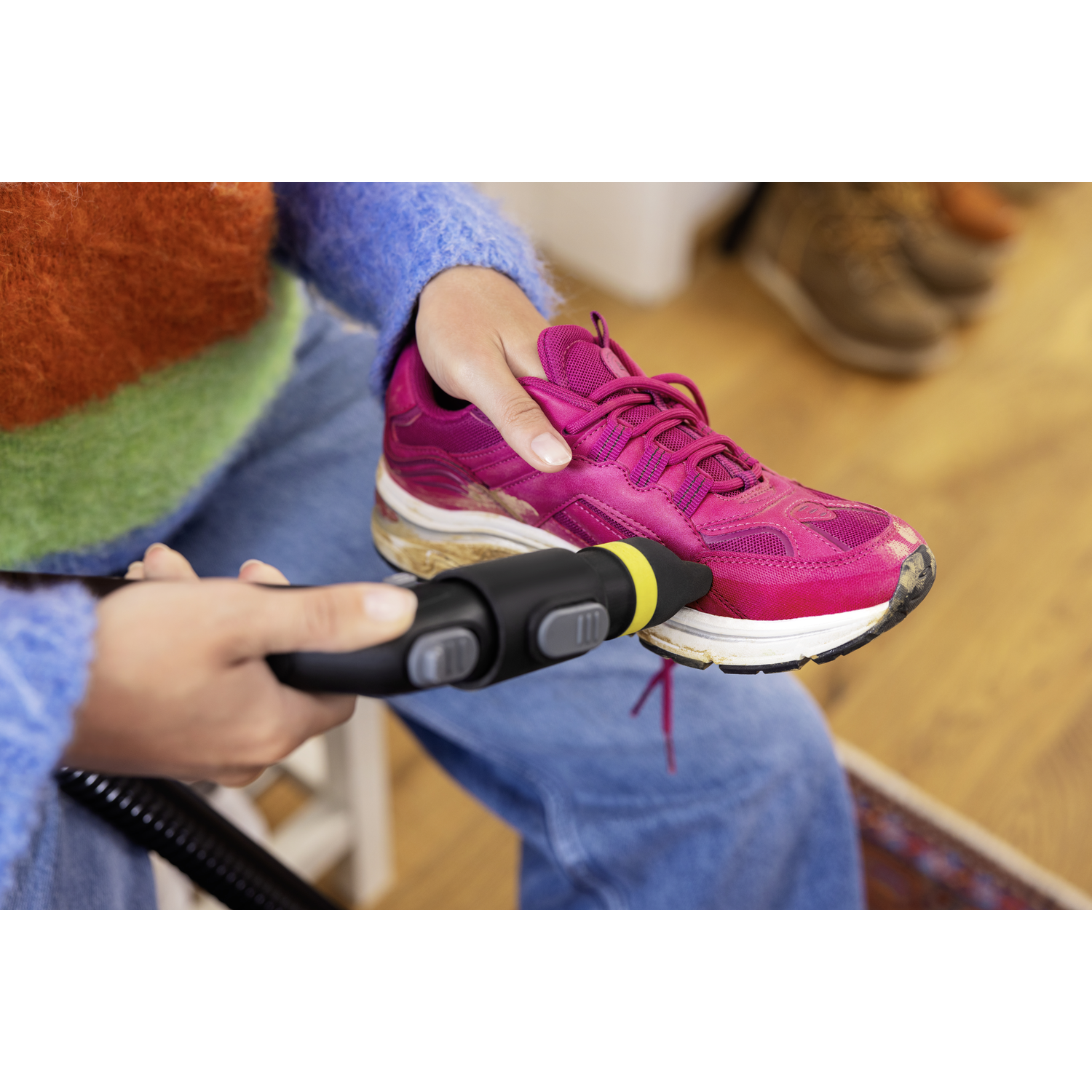 Een persoon maakt een roze hardloopschoen schoon met een zwart-geel schoonmaakapparaat. De schoen ligt op de schoot van de persoon.