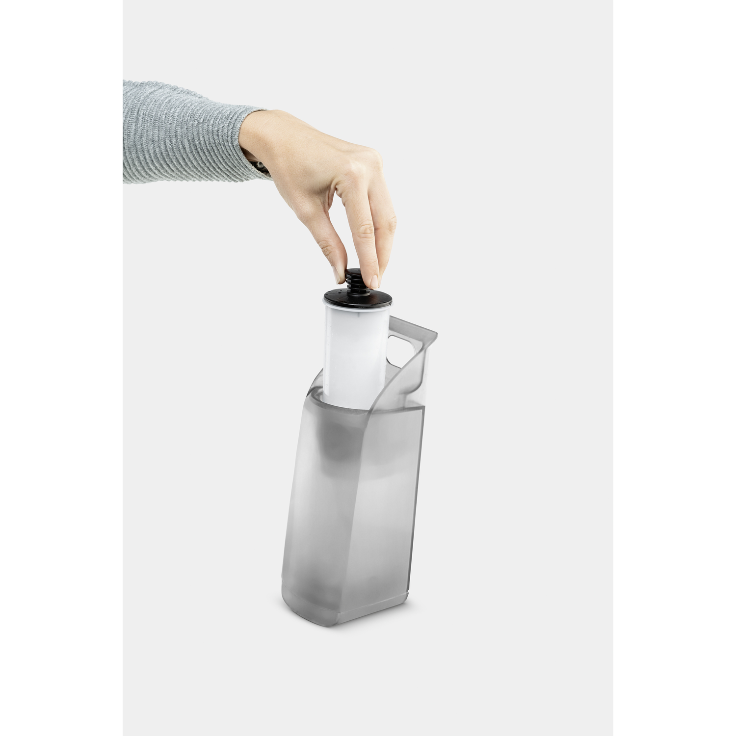 Een hand plaatst een wit filter in een grijze container. De achtergrond is wit.
