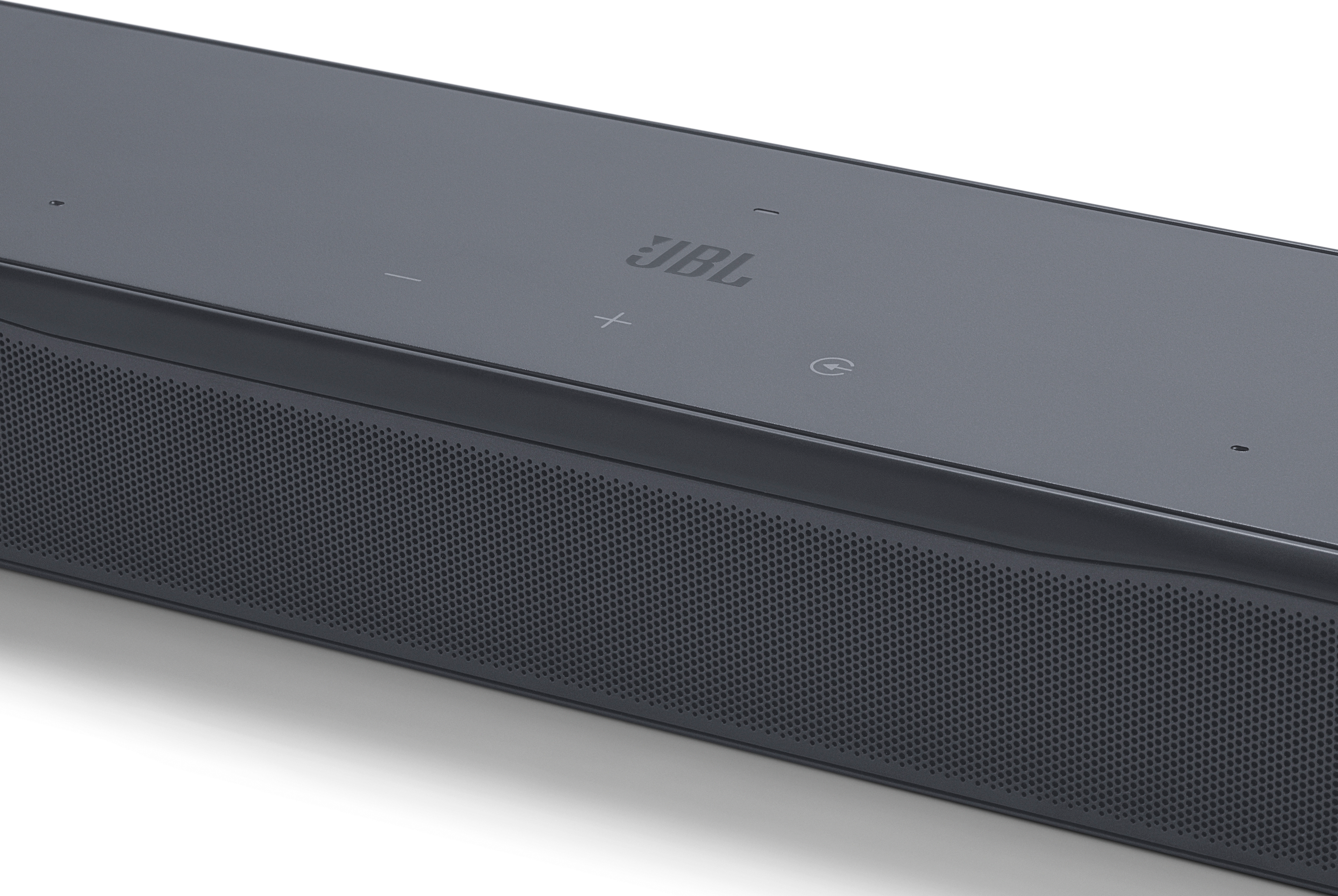 Primo piano di una soundbar JBL grigio scuro. La parte superiore ha pulsanti di controllo e il logo JBL. La parte anteriore ha una griglia per altoparlanti perforata.