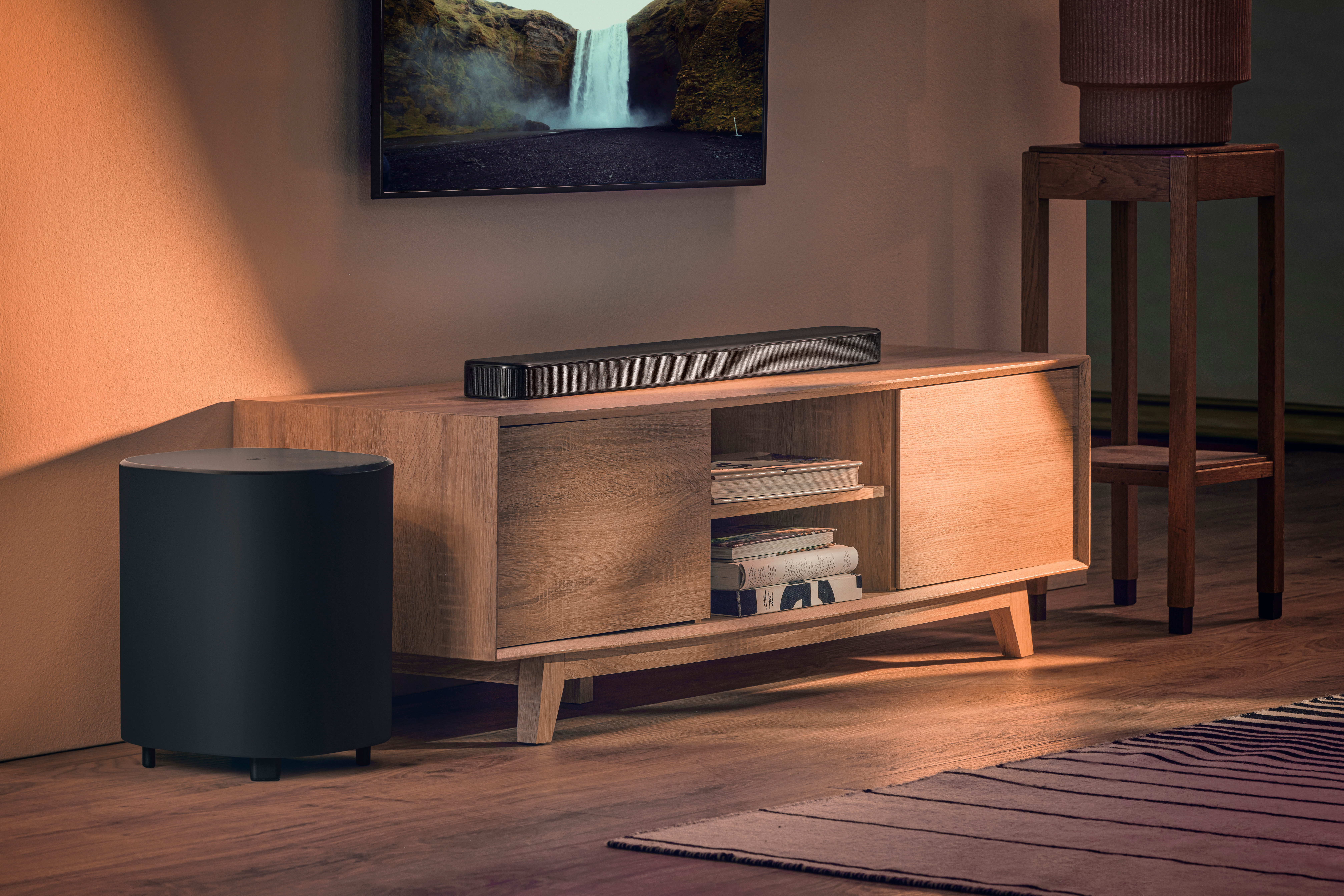Un soggiorno con una TV che mostra una cascata. C'è una soundbar, un subwoofer, un mobile in legno e un tavolino.