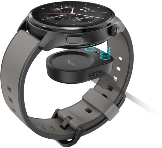 Smartwatch z czarną tarczą i szarym paskiem. Zegarek znajduje się na stacji ładującej. Stacja posiada port USB-C.
