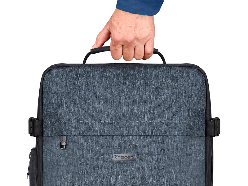 Ręka trzyma ciemnoszary plecak z czarną rączką. Plecak ma srebrny zamek błyskawiczny i klamrę z boku.