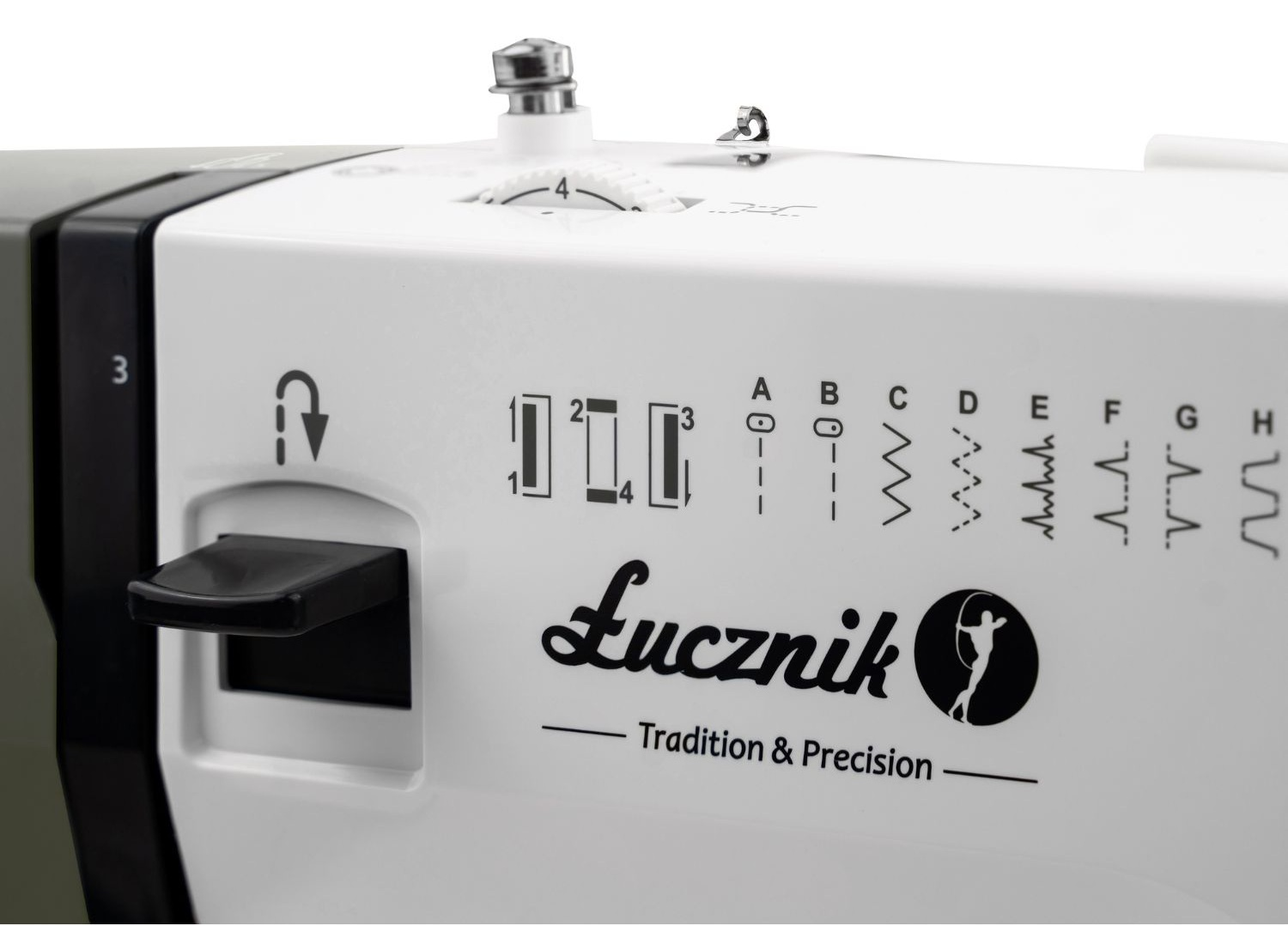 Zbliżenie białej maszyny do szycia. Zawiera ustawienia, wzory ściegów, czarną dźwignię i logo 'Łucznik' z napisem 'Tradition & Precision'.
