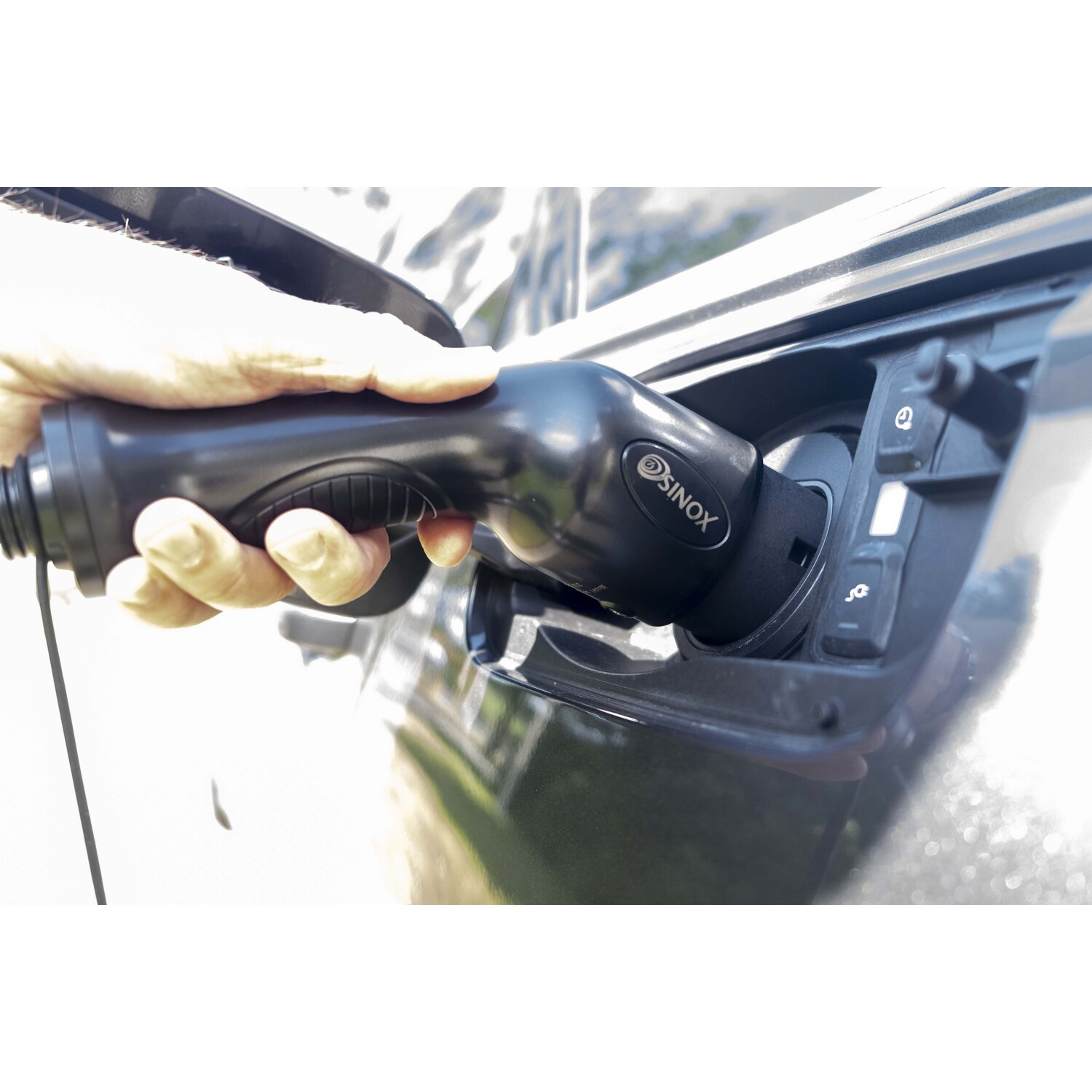 Une main branchant un câble de chargement noir dans le port de chargement d'une voiture. Le chargeur porte le logo SINOL.