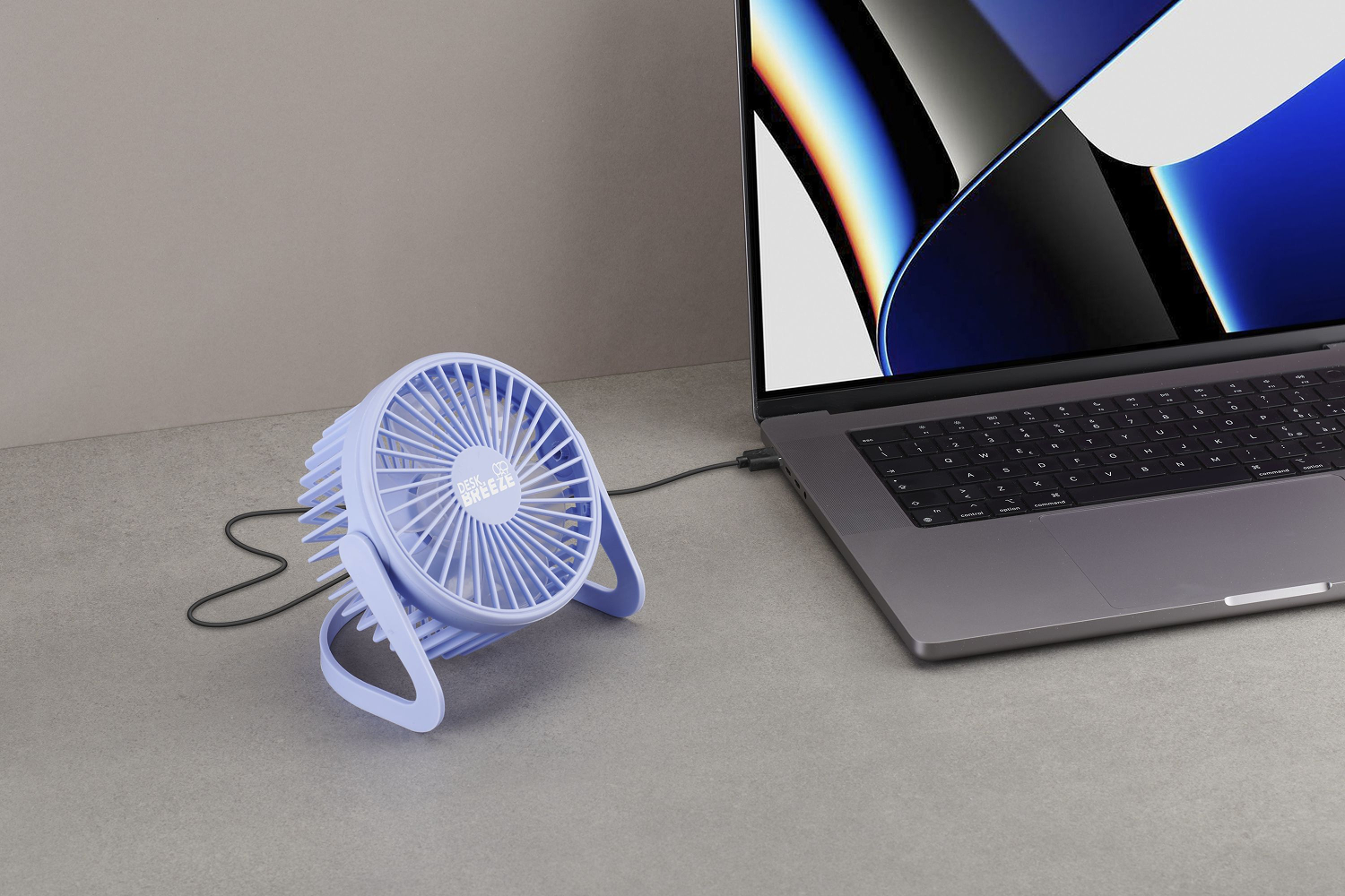 Un ventilador de escritorio morado claro está junto a una computadora portátil. El ventilador está conectado a la computadora portátil. El fondo es una superficie gris.