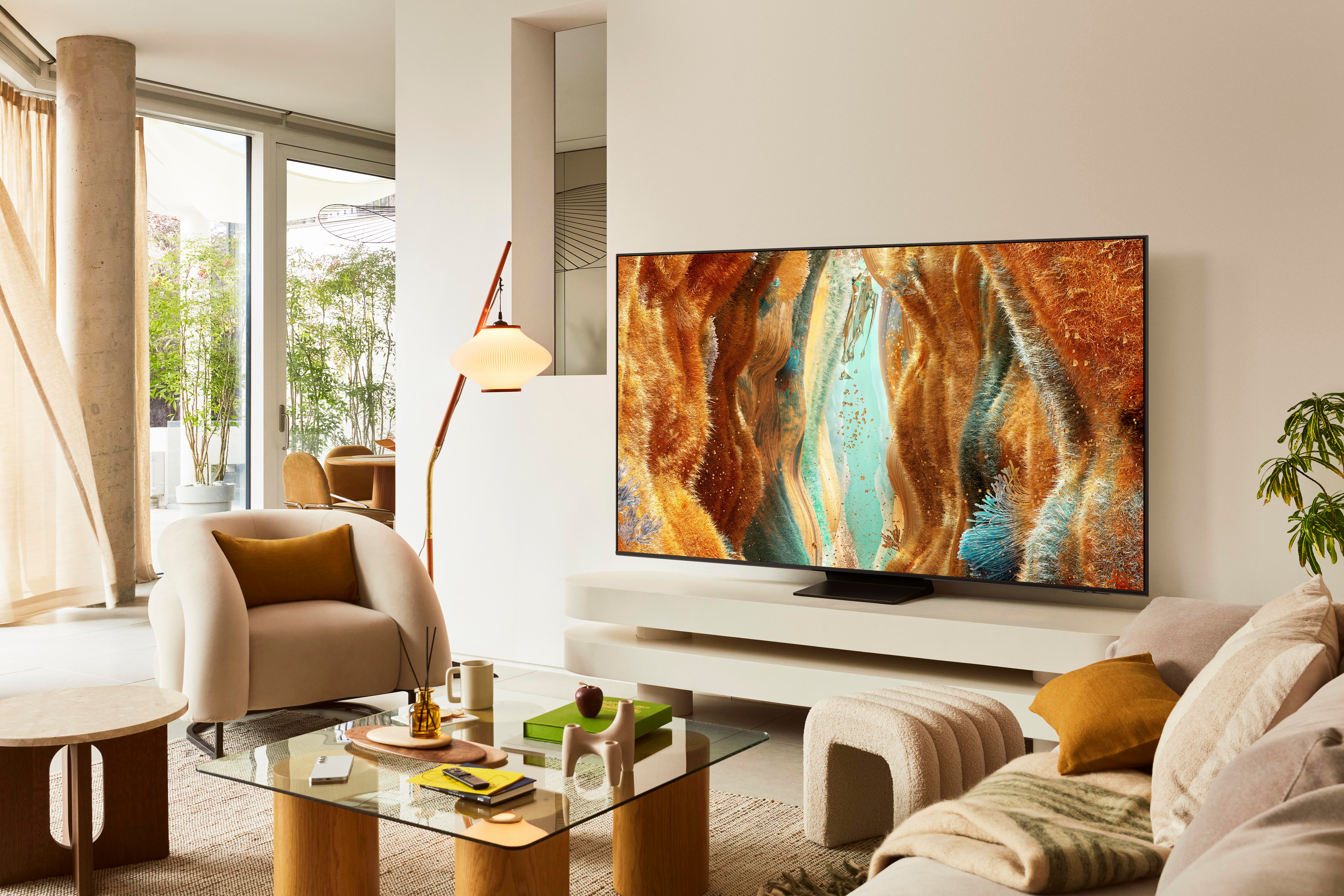 Wohnzimmer mit TV, der abstrakte Kunst zeigt. Beige Sofa, Sessel, Glastisch. Stehlampe, kleine Beistelltische und Außenansicht.