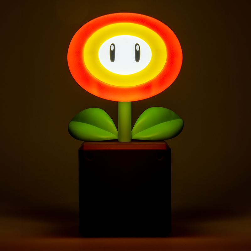 Eine Mario-Feuerblumen-Lampe. Es ist eine rot-gelbe Blume mit einem Gesicht, grünen Blättern und steht in einem braunen Topf.