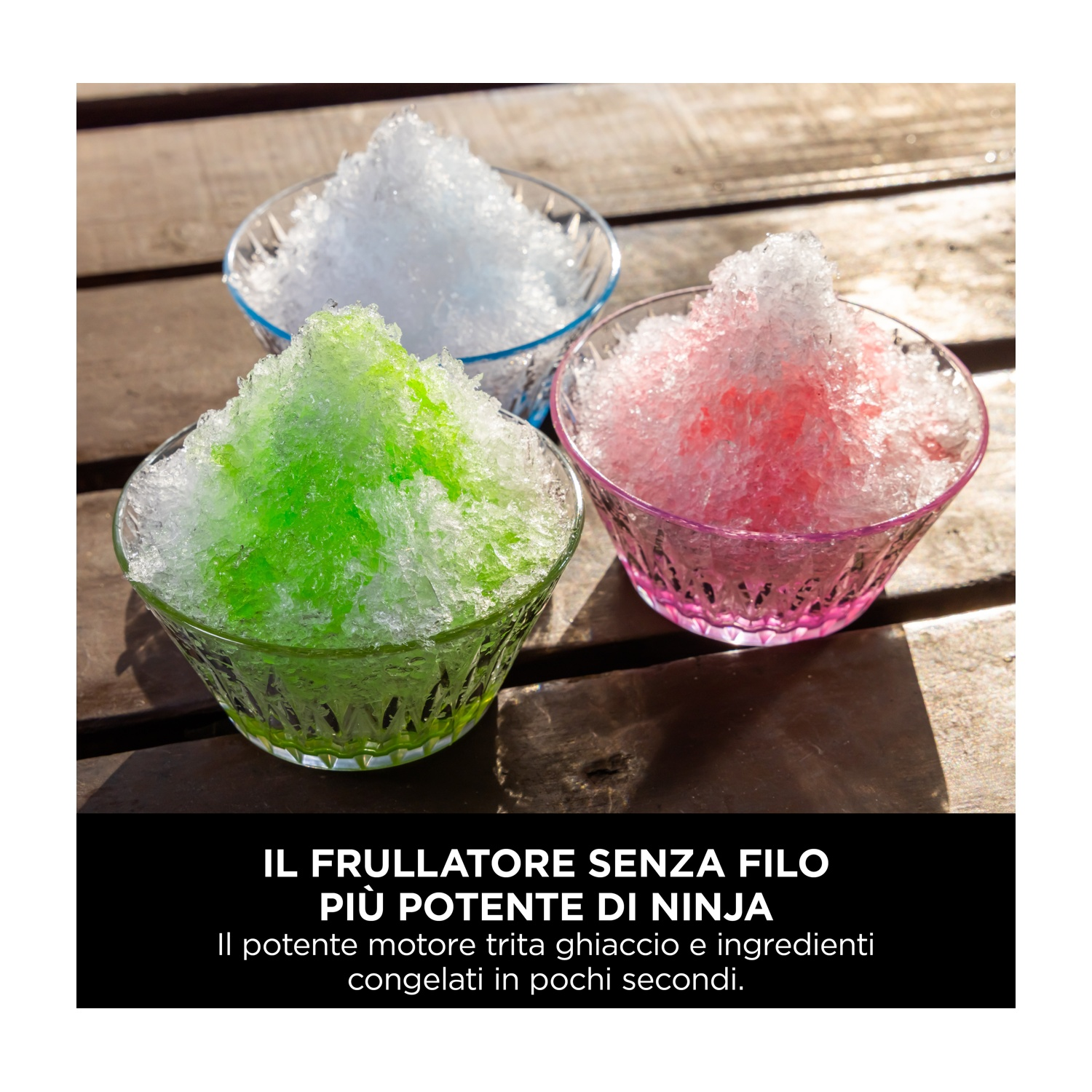 Tre ciotole di vetro riempite di ghiaccio tritato verde, rosa e bianco. Sono su un tavolo di legno. Il testo sottostante pubblicizza un frullatore.