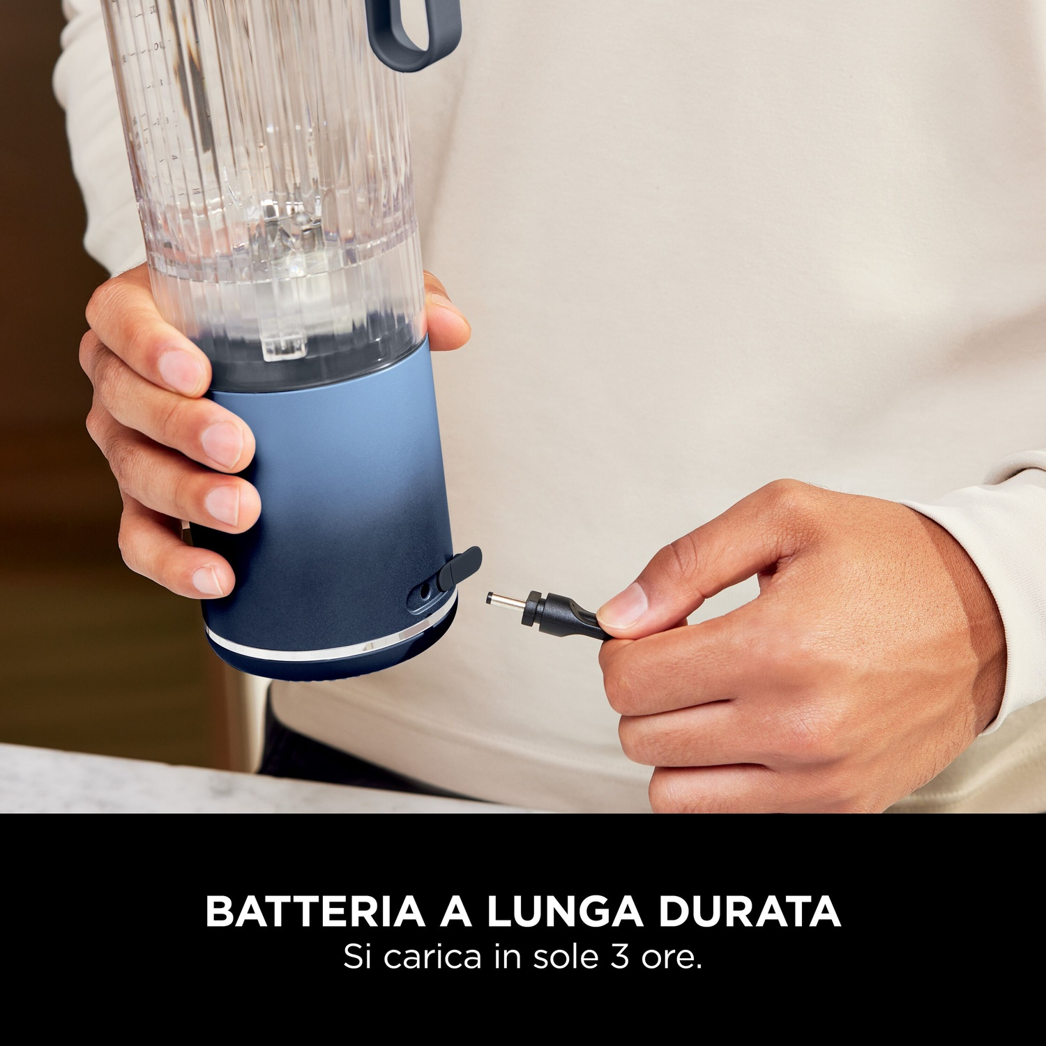 Persona che tiene in mano un frullatore blu e un cavo di ricarica. Il frullatore è parzialmente assemblato. Testo in basso: 'Batteria a lunga durata'.