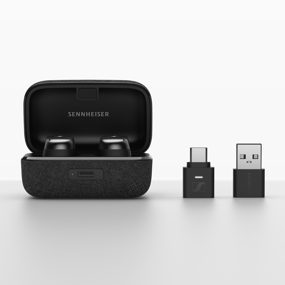 Fekete Sennheiser fülhallgató töltőtokban, USB-C és USB-A adapterekkel. Mindez fehér háttéren.